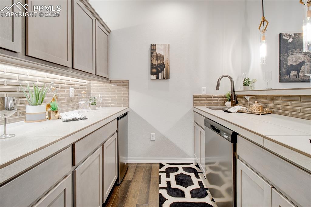 Kitchen featuring tasteful backsplash, stainless steel dishwasher, hanging light fixtures, and dark wood-style floors