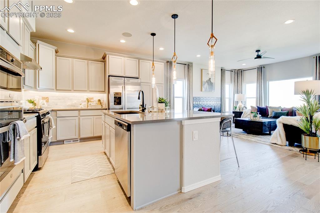 Kitchen featuring backsplash, a kitchen island with sink, stainless steel appliances, decorative light fixtures, and open floor plan
