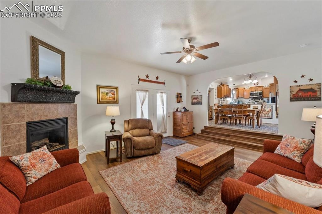 Living area with wood finished floors, arched walkways, a fireplace, and a ceiling fan