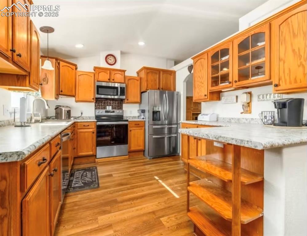 Kitchen featuring pendant lighting, appliances with stainless steel finishes, light wood-style flooring, brown cabinets, and lofted ceiling