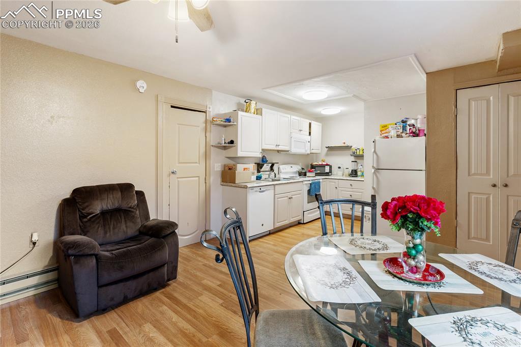 The dining area features light wood-style floors and a ceiling fan, overlooking the kitchen!