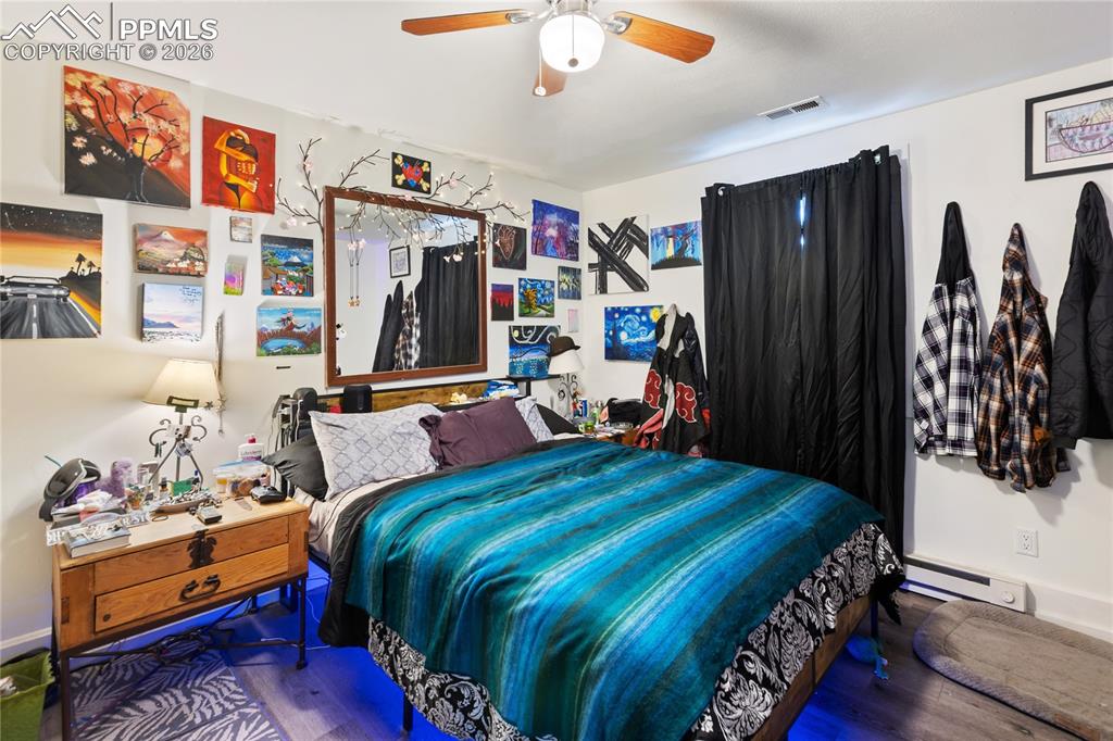 The main bedroom with a baseboard heating unit, wood finished floors, and ceiling fan!