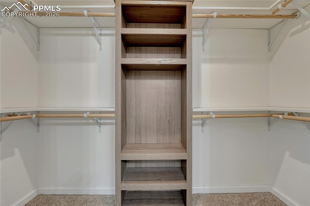 Large primary walk-in closet with dual wrap around shelves and poles along with a built-in center shelving unit

