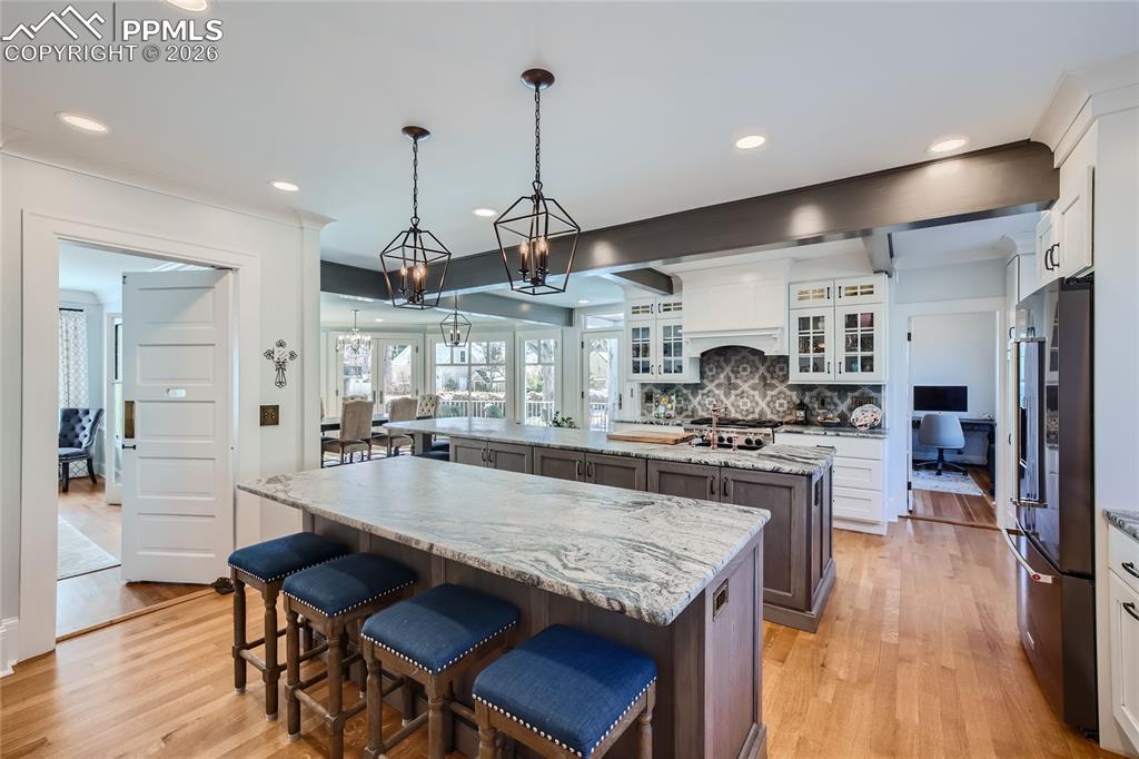 Kitchen with white cabinets, backsplash, light wood flooring, two kitchen island, and hanging light fixtures