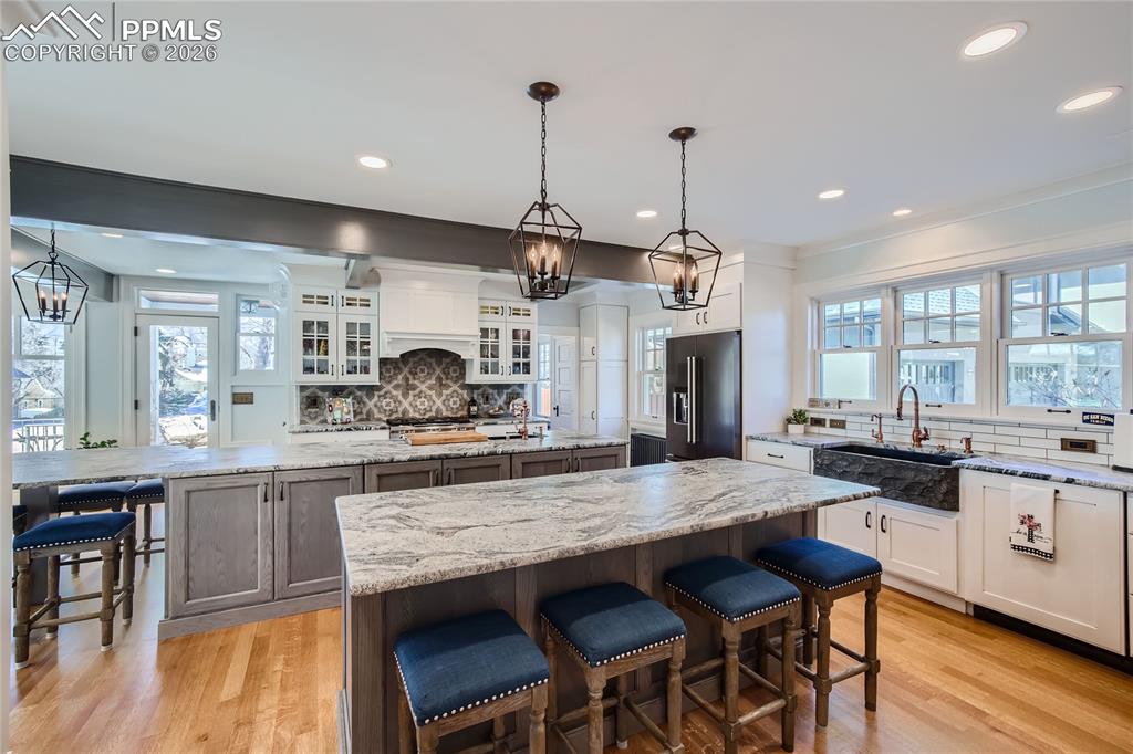 Kitchen with light hardwood flooring, a kitchen island, white and gray cabinetry, tasteful backsplash, and high end refrigerator