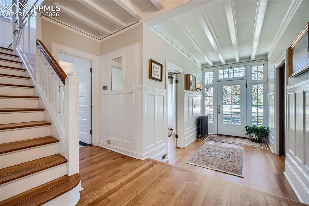 Foyer featuring beam ceiling, light wood flooring, and crown molding