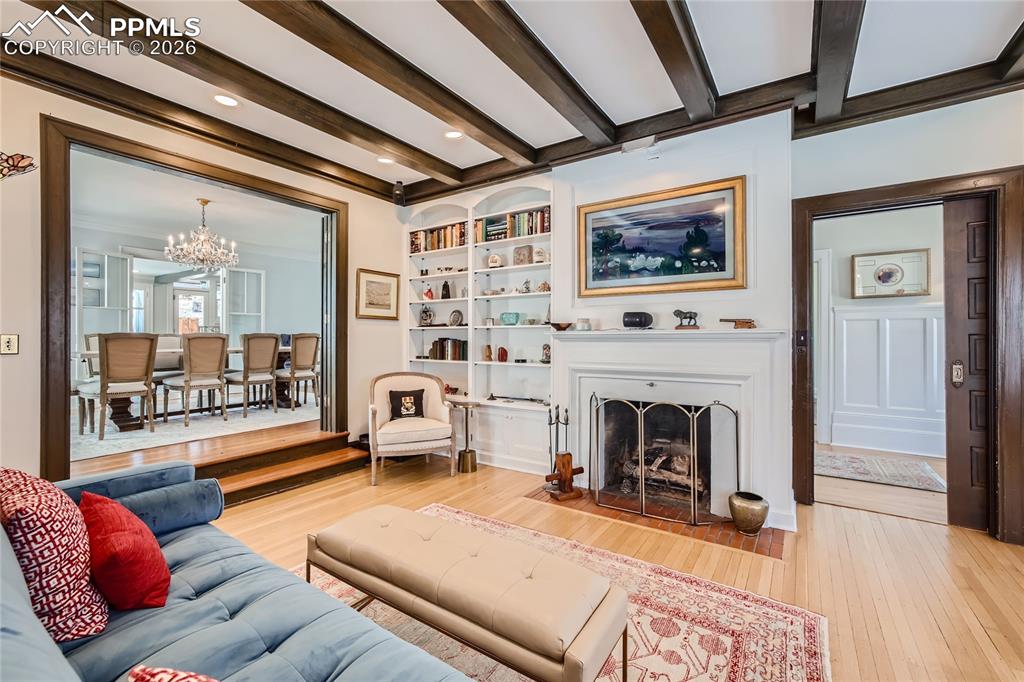 Living room with crown molding, light wood-type flooring, and beamed ceiling