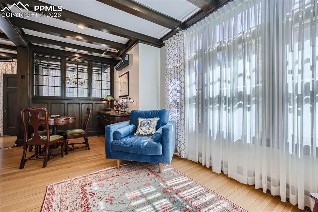 Living area with a wall mounted air conditioner, light hardwood / wood-style flooring, and beamed ceiling