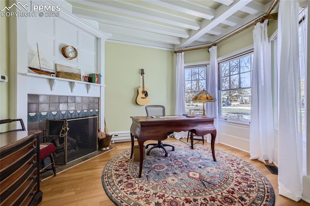 Office space with a baseboard radiator, light hardwood / wood-style floors, beam ceiling, and a tile fireplace