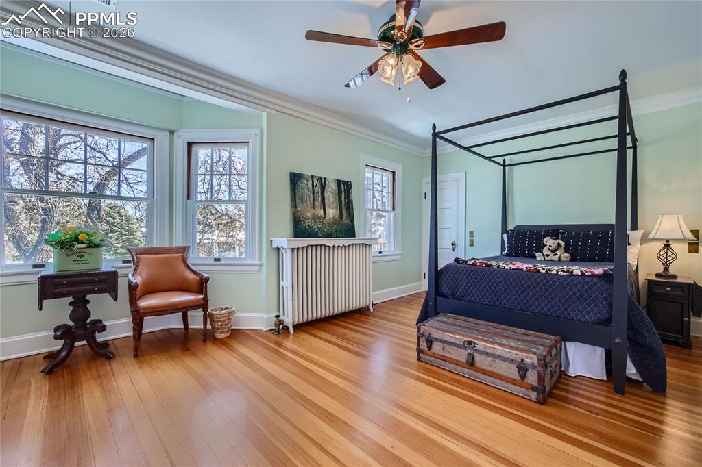 Bedroom with radiator, light hardwood floors, ornamental molding, and ceiling fan