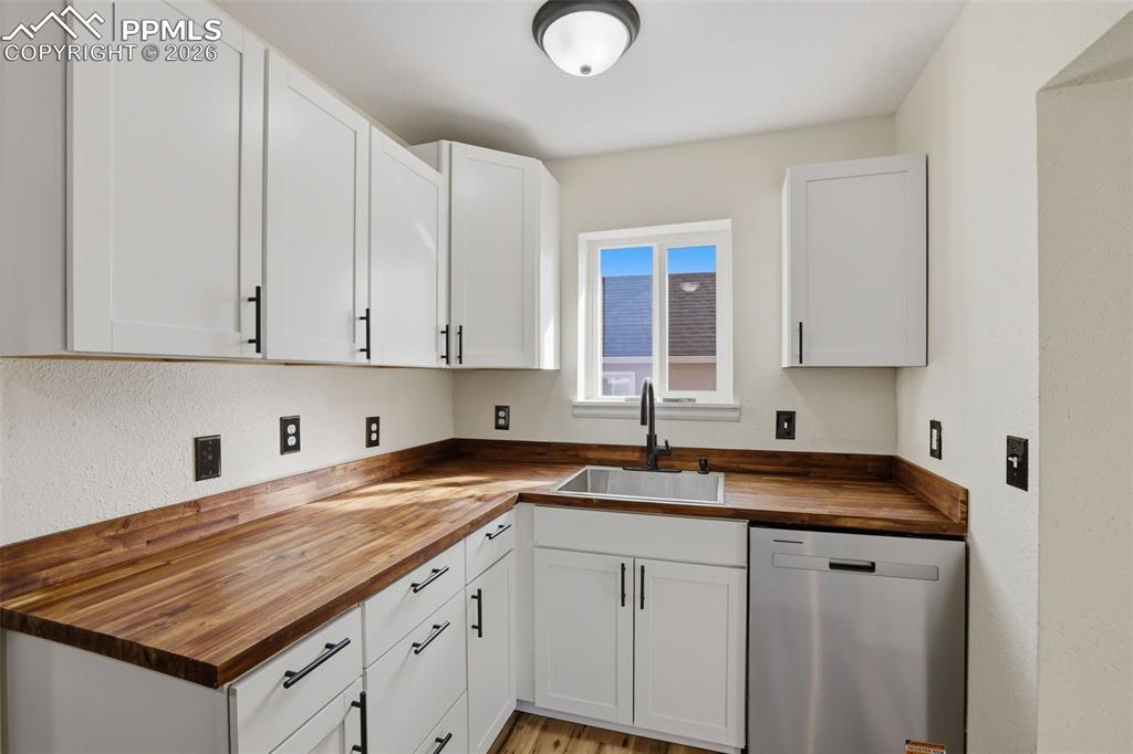 Kitchen featuring butcher block countertops, dishwasher, white cabinets, and light wood-style floors