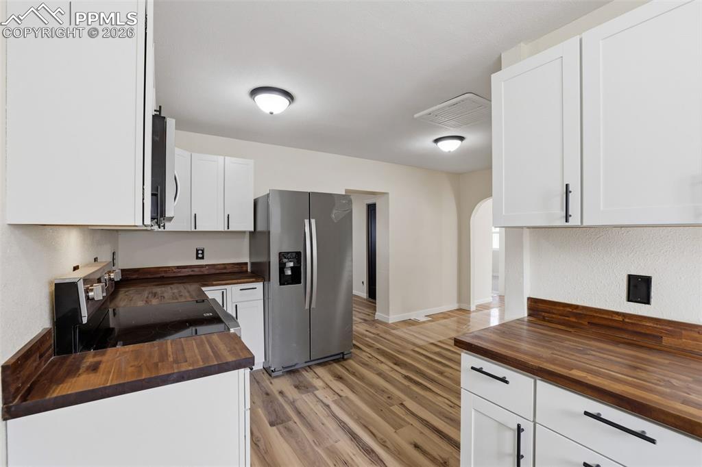 Kitchen with butcher block counters, stainless steel appliances, white cabinets, light wood-style flooring, and arched walkways