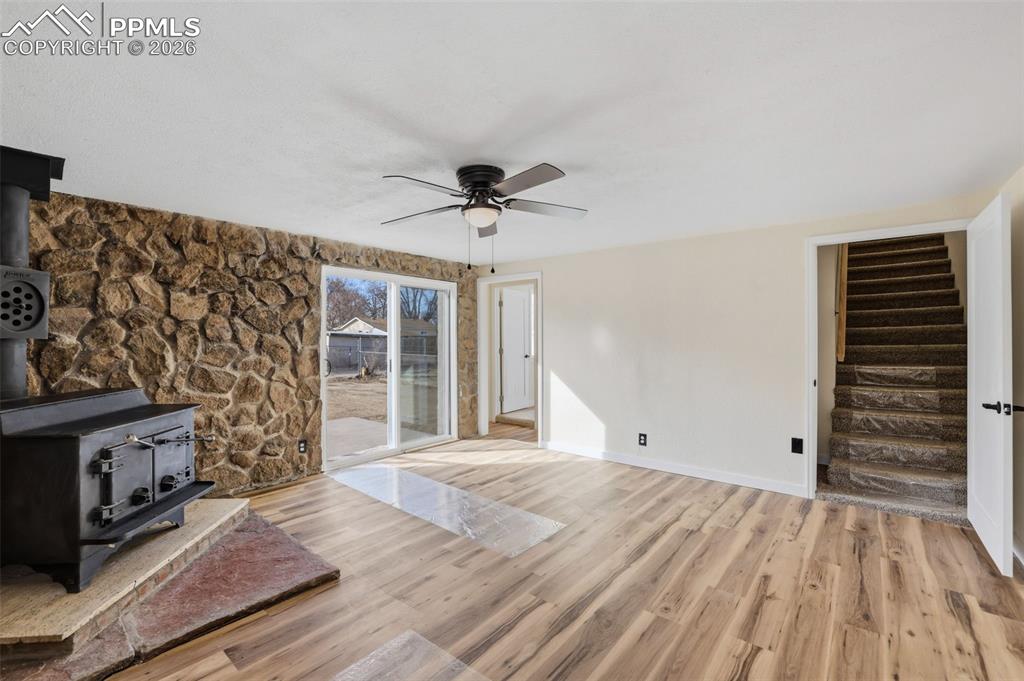 Unfurnished living room with a wood stove, a ceiling fan, and light wood-style floors
