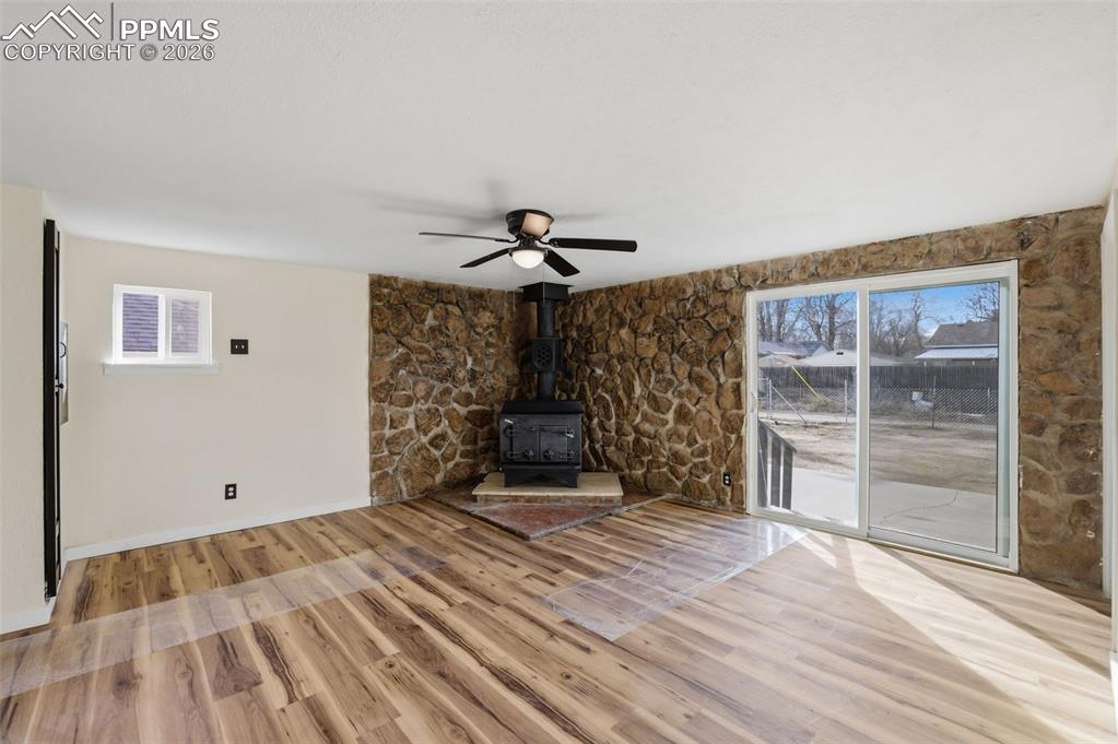 Unfurnished living room with a wood stove, plenty of natural light, light wood-style flooring, and ceiling fan