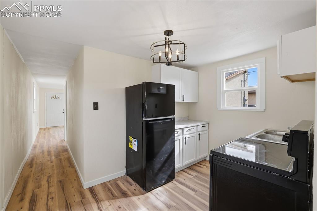 Kitchen featuring freestanding refrigerator, white cabinetry, light countertops, and light wood-style flooring