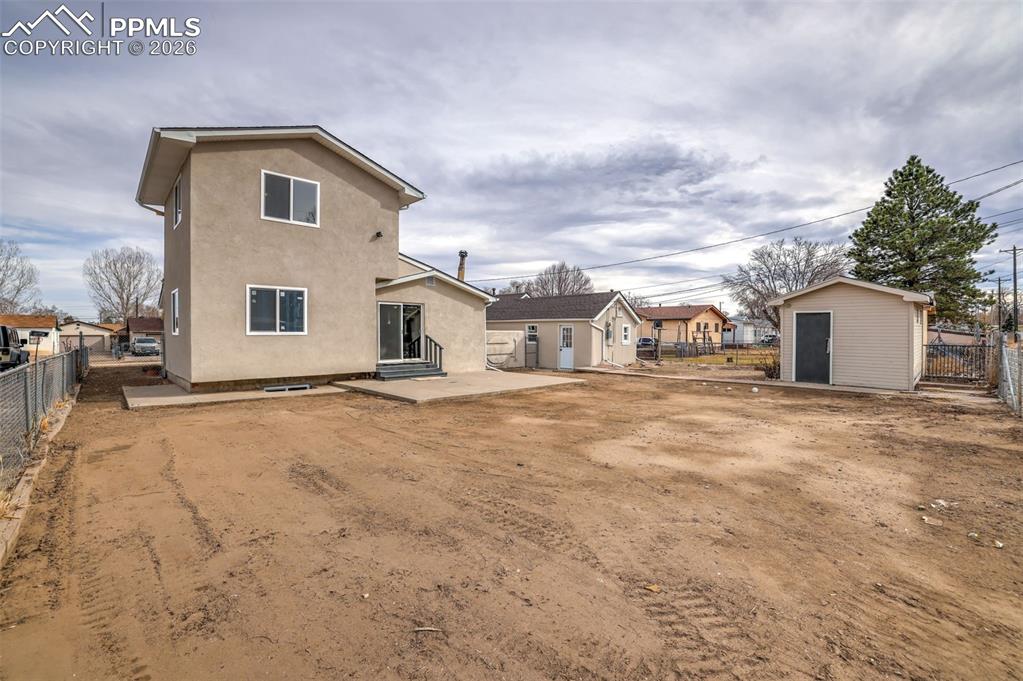 Back of house with a fenced backyard, stucco siding, a patio, a storage unit, and a residential view