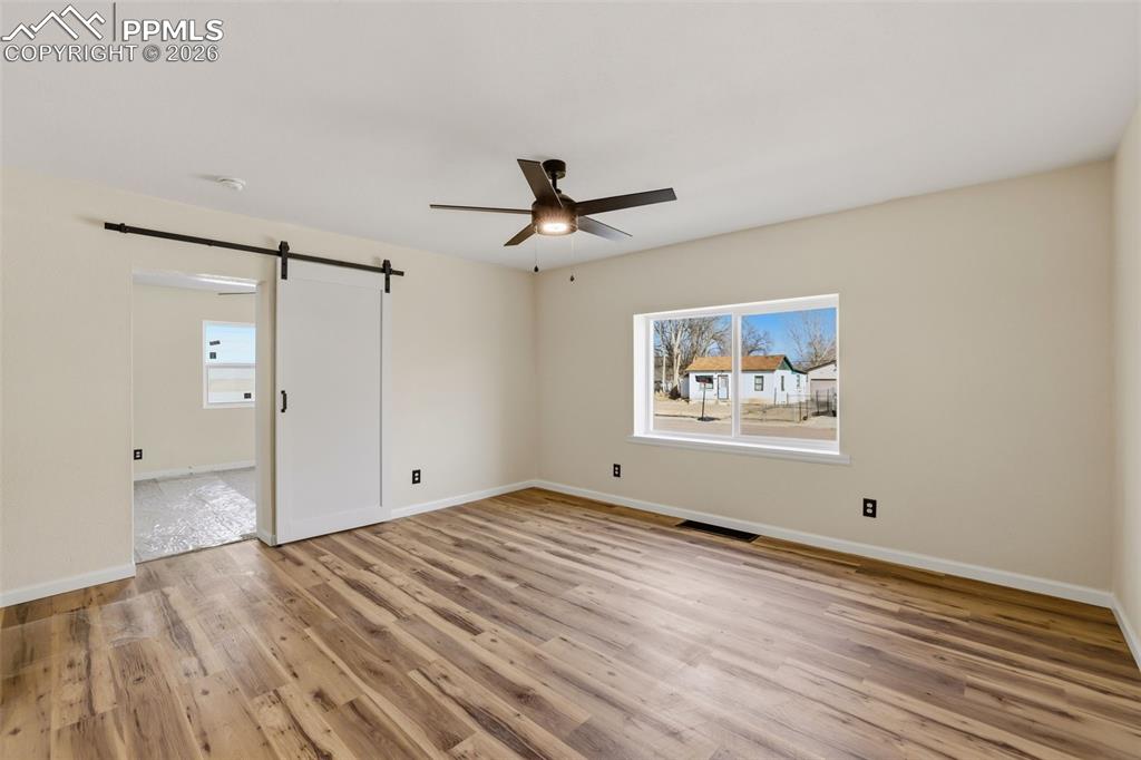 Spare room featuring a barn door, ceiling fan, light wood-type flooring, and plenty of natural light