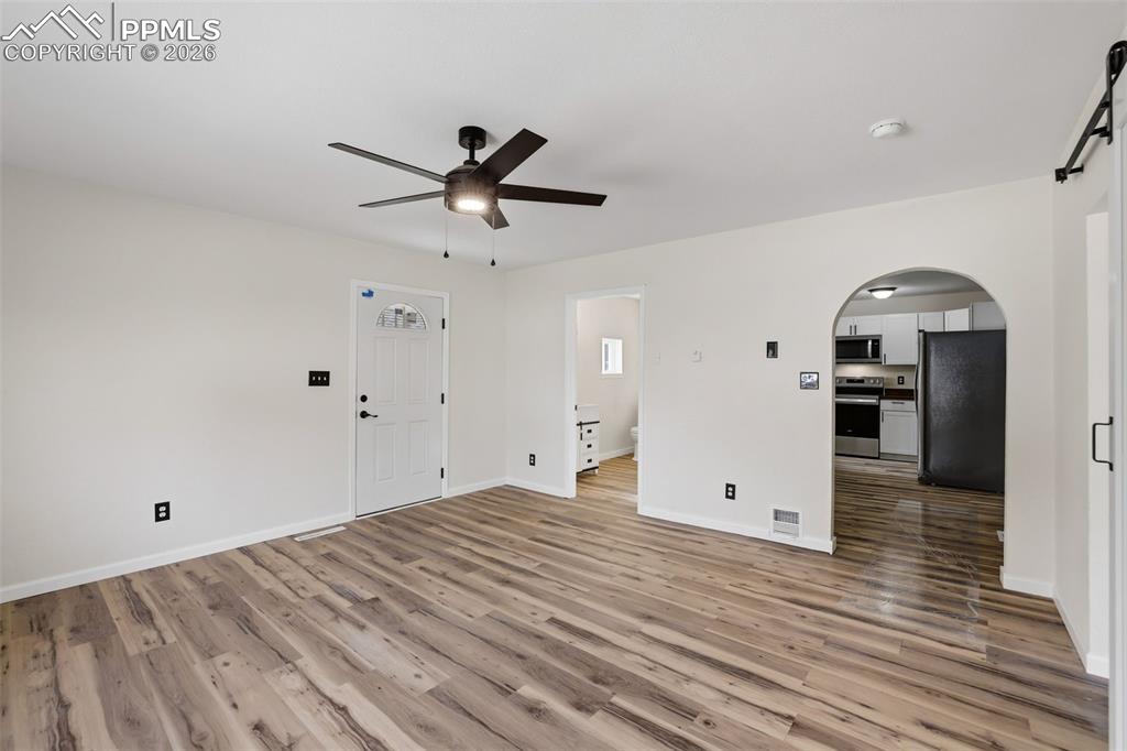 Unfurnished living room featuring arched walkways, a barn door, ceiling fan, and light wood-style flooring