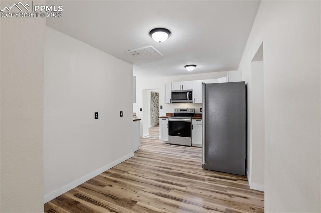 Kitchen with stainless steel appliances, white cabinetry, and light wood-style flooring