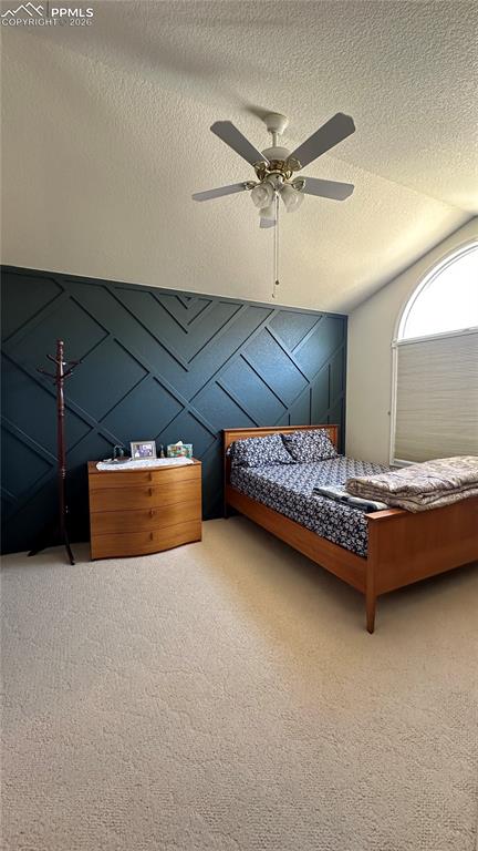 Carpeted bedroom with lofted ceiling, ceiling fan, and a textured ceiling