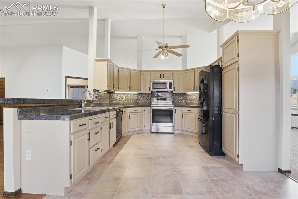 Kitchen featuring high vaulted ceiling, black appliances, cream cabinets, tasteful backsplash, and a peninsula
