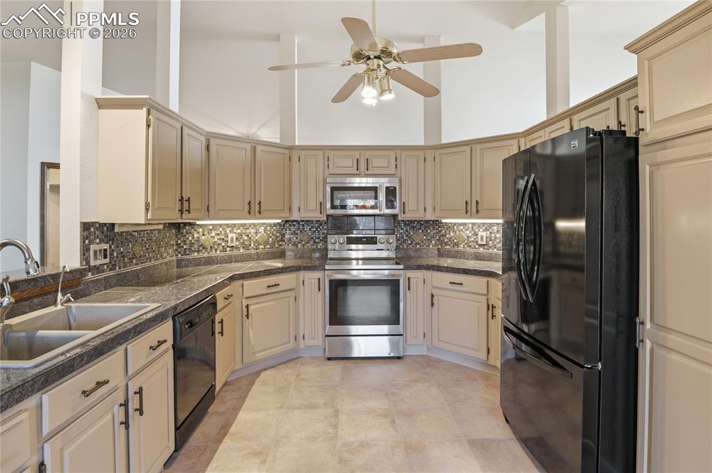 Kitchen featuring black appliances, tile countertops, a towering ceiling, tasteful backsplash, and a ceiling fan