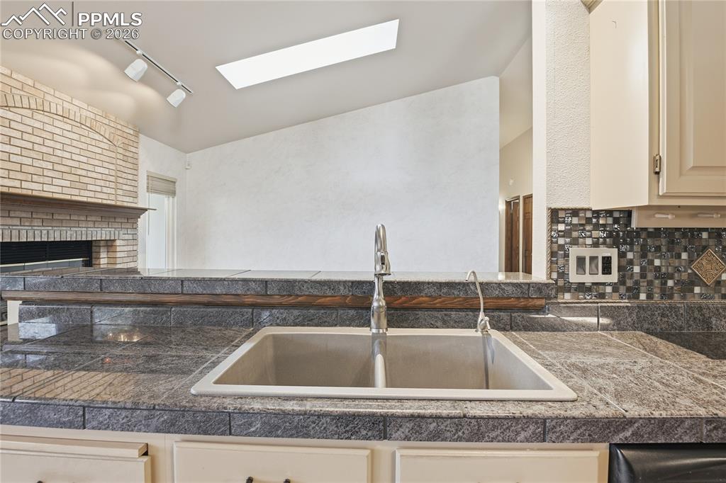 Kitchen with tile counters, track lighting, a skylight, cream cabinetry, and a fireplace