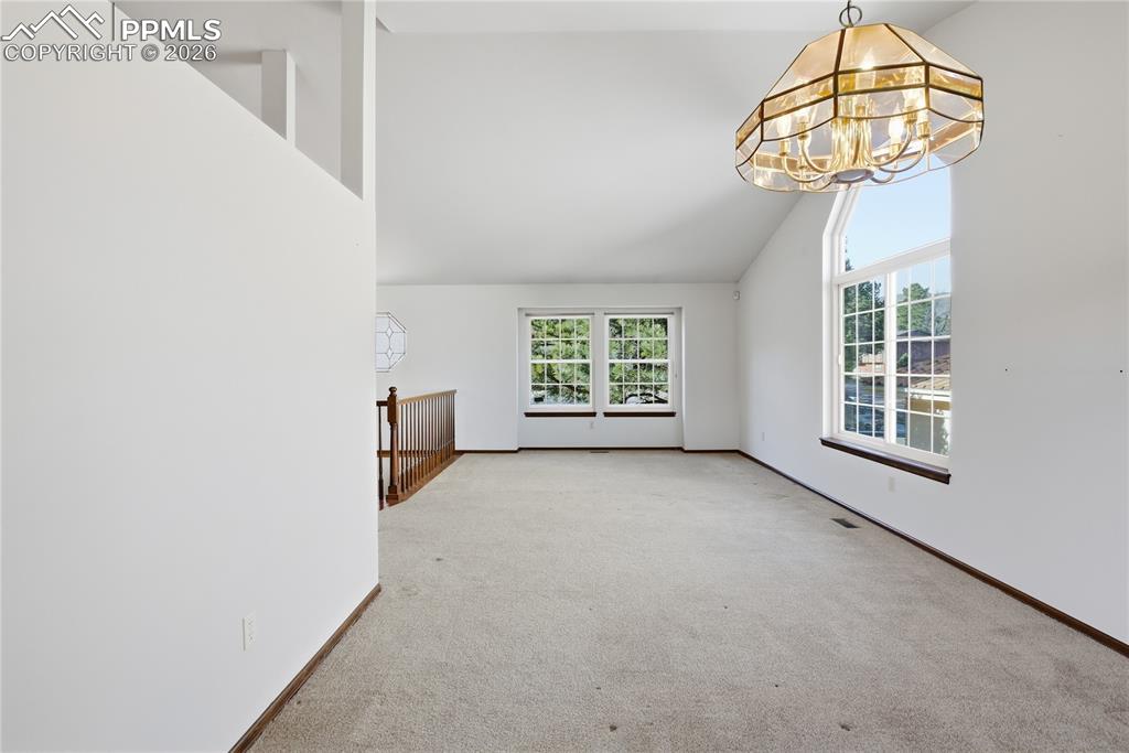Spare room with carpet, a chandelier, and high vaulted ceiling