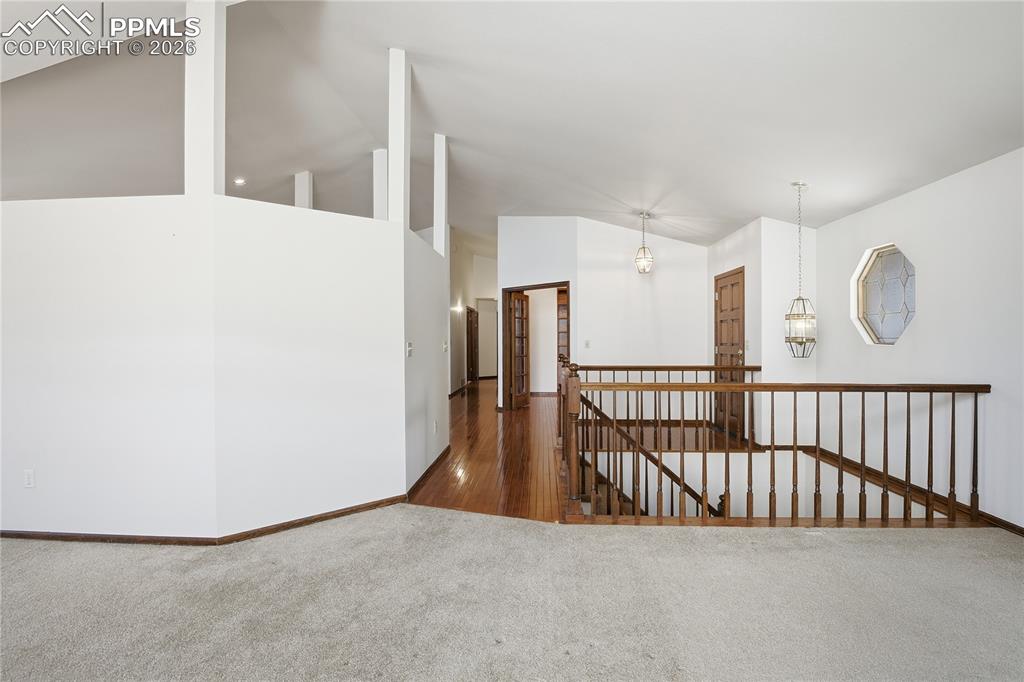 Hall featuring dark colored carpet, an upstairs landing, and high vaulted ceiling