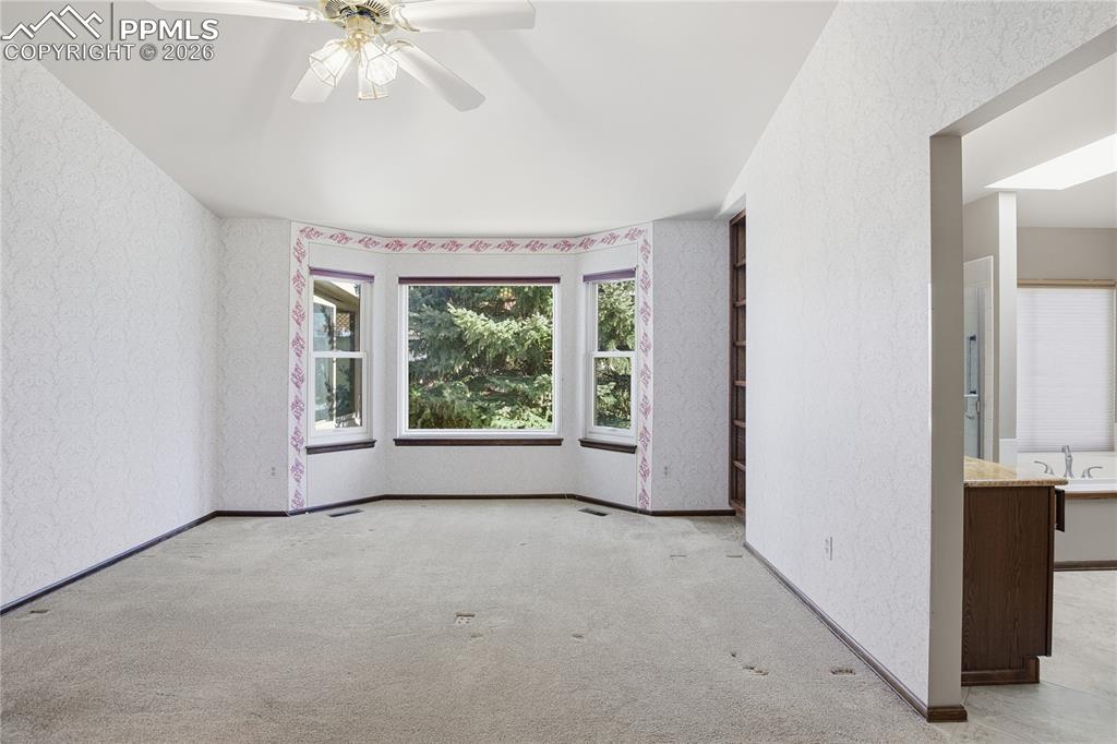 Carpeted empty room featuring a textured wall, ceiling fan, and wallpapered walls