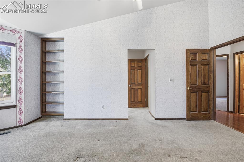 Unfurnished bedroom with wallpapered walls, vaulted ceiling, and carpet flooring