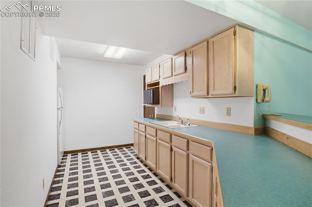 Kitchen with light brown cabinets, light countertops, freestanding refrigerator, and light floors