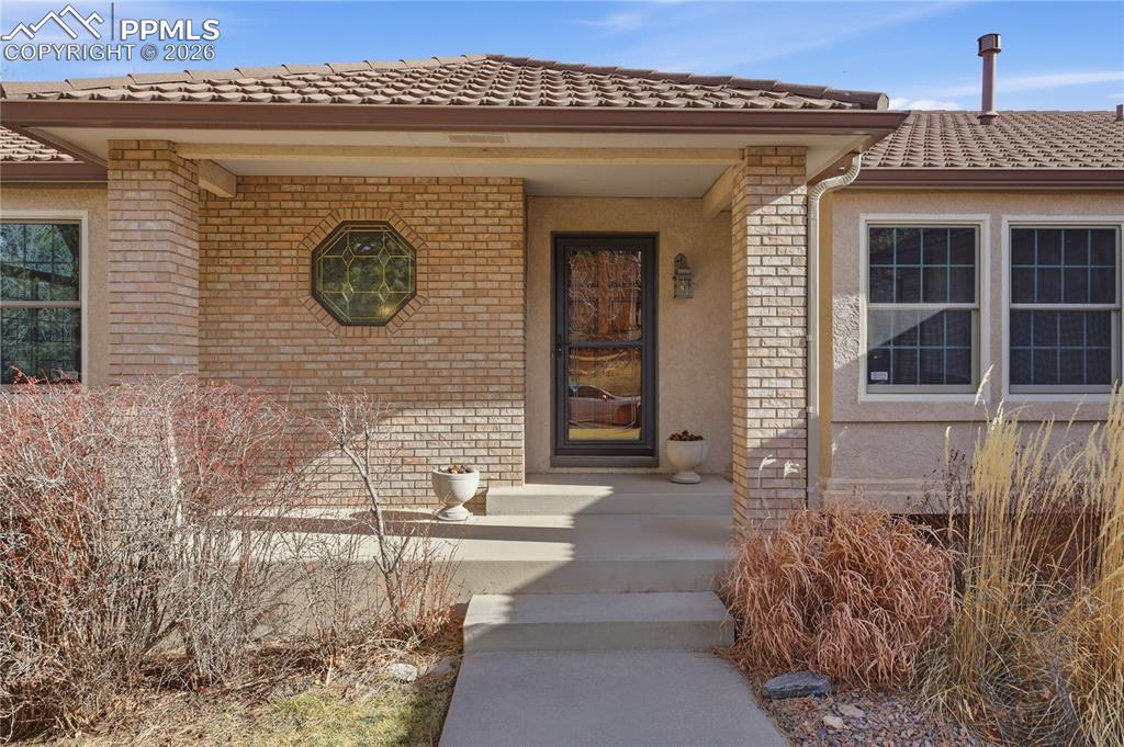 Doorway to property featuring brick siding, a tile roof, and stucco siding