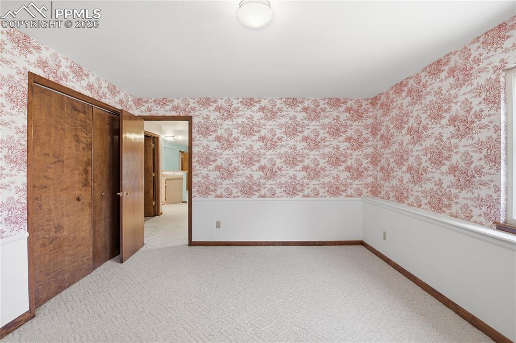 Unfurnished room with wallpapered walls, light carpet, and wainscoting