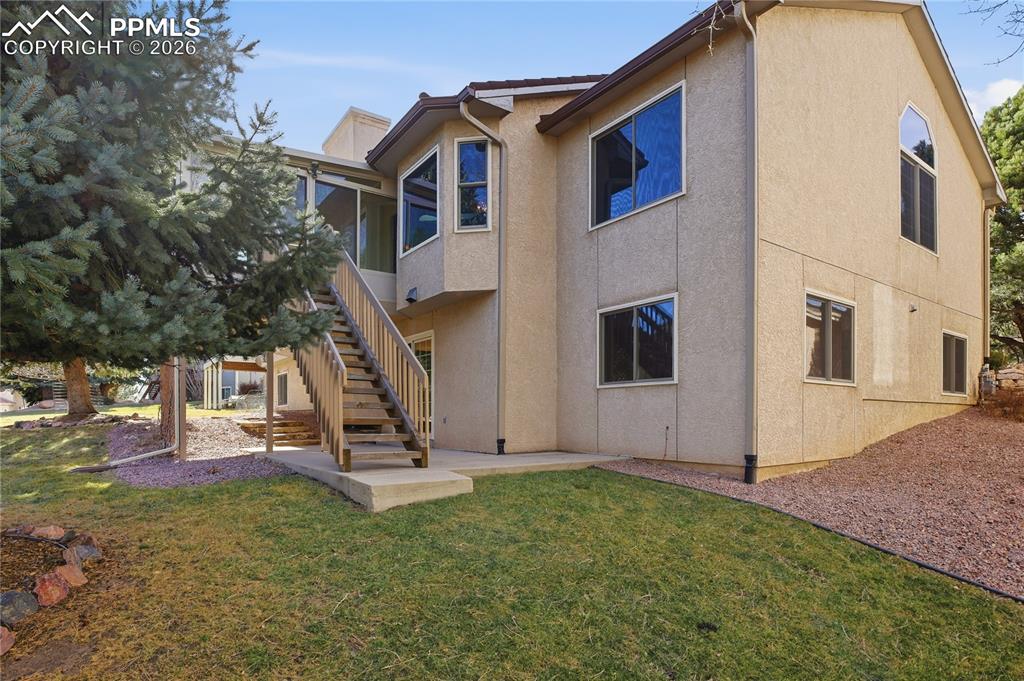 Back of house featuring stairs, a yard, and stucco siding
