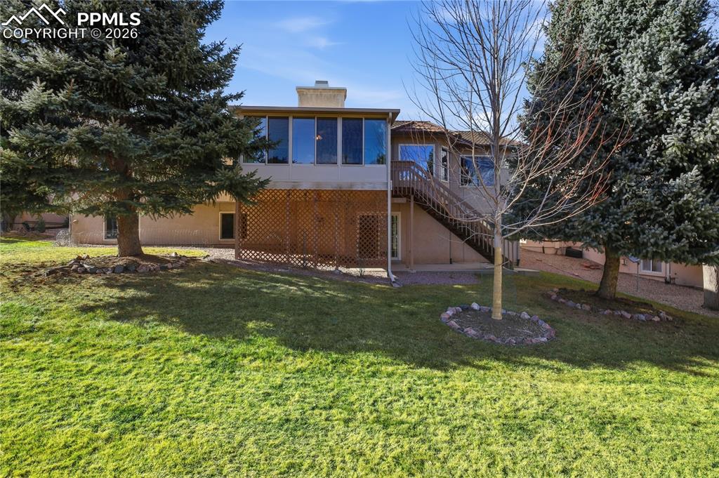 Back of property with a chimney, a wooden deck, stairway, a lawn, and a patio