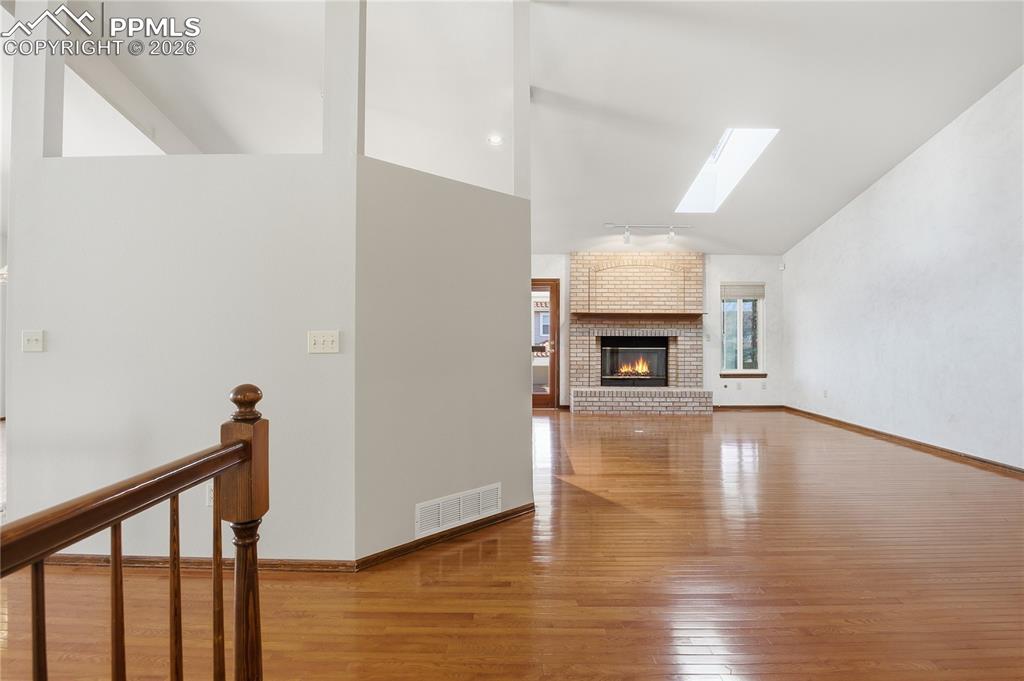 Unfurnished living room featuring a skylight, light wood finished floors, a brick fireplace, and high vaulted ceiling