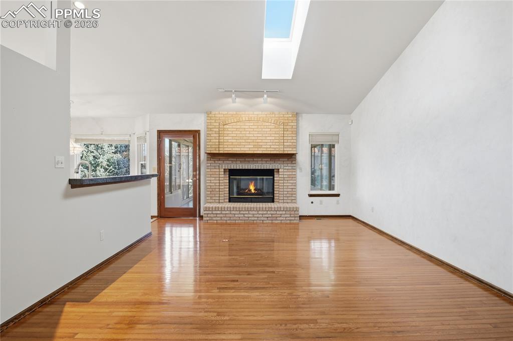Unfurnished living room featuring a skylight, a fireplace, light wood-type flooring, rail lighting, and vaulted ceiling