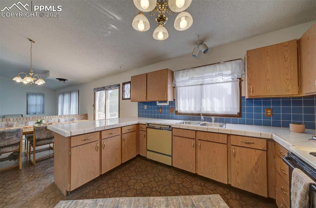 The Kitchen features vinyl flooring, a pantry, wood cabinetry, tile countertops, & a breakfast bar.