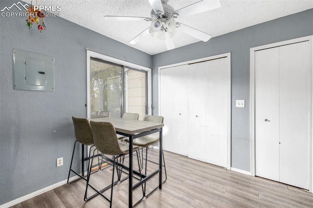 Dining space featuring a textured wall, a textured ceiling, wood finished floors, electric panel, and ceiling fan