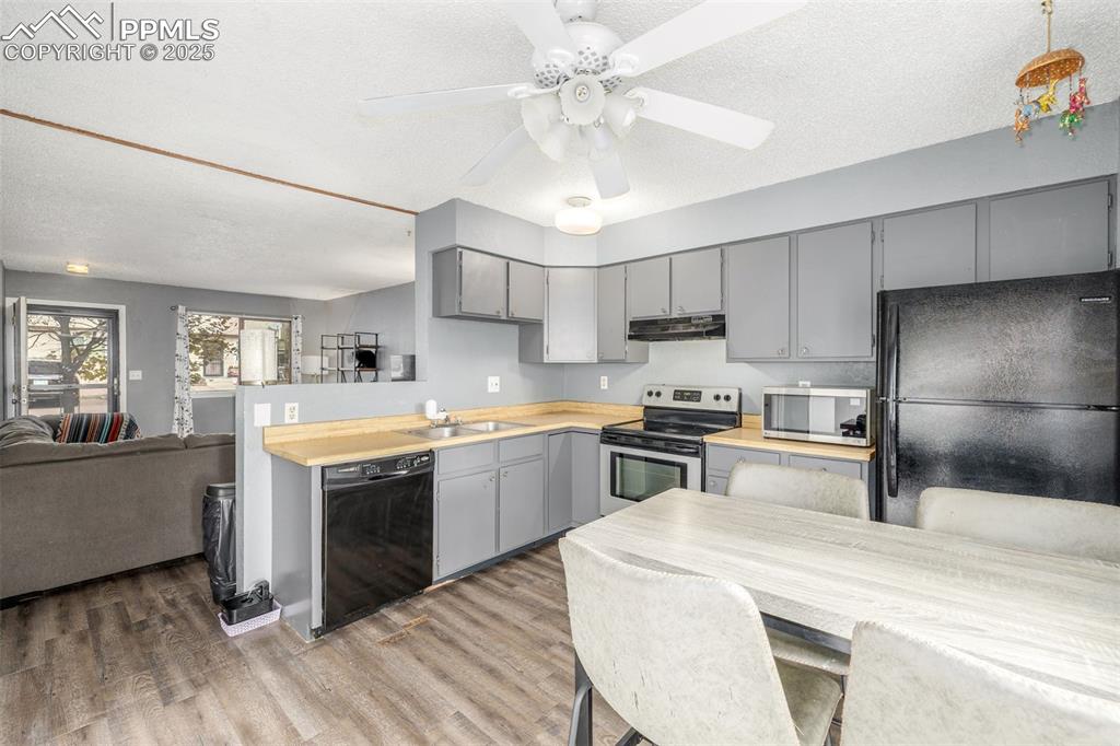 Kitchen with gray cabinetry, black appliances, open floor plan, a textured ceiling, and light countertops