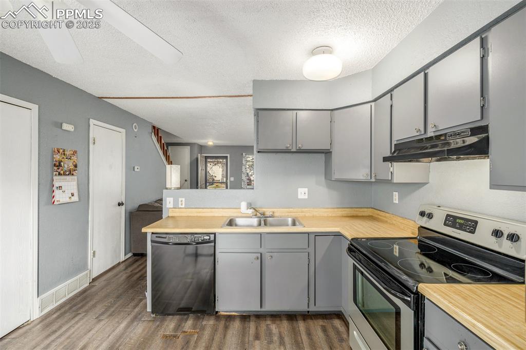 Kitchen with gray cabinetry, stainless steel range with electric stovetop, a textured ceiling, dark wood-type flooring, and black dishwasher