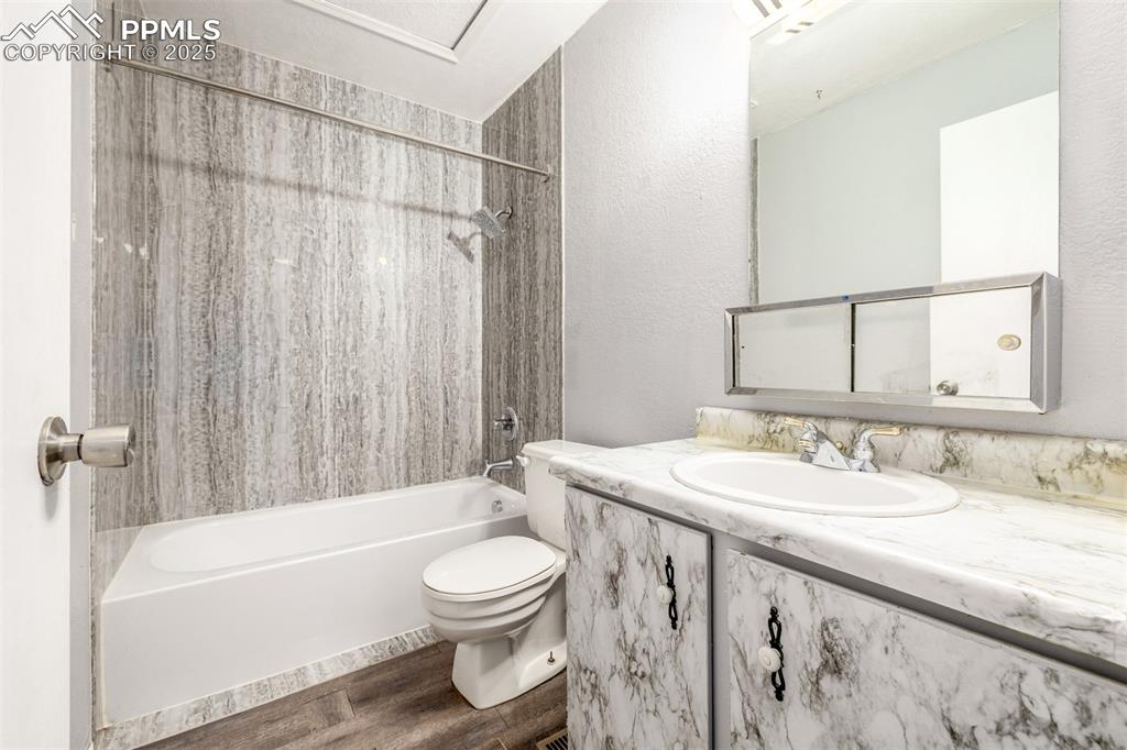Full bathroom with dark wood-style floors, shower / tub combo with curtain & vanity