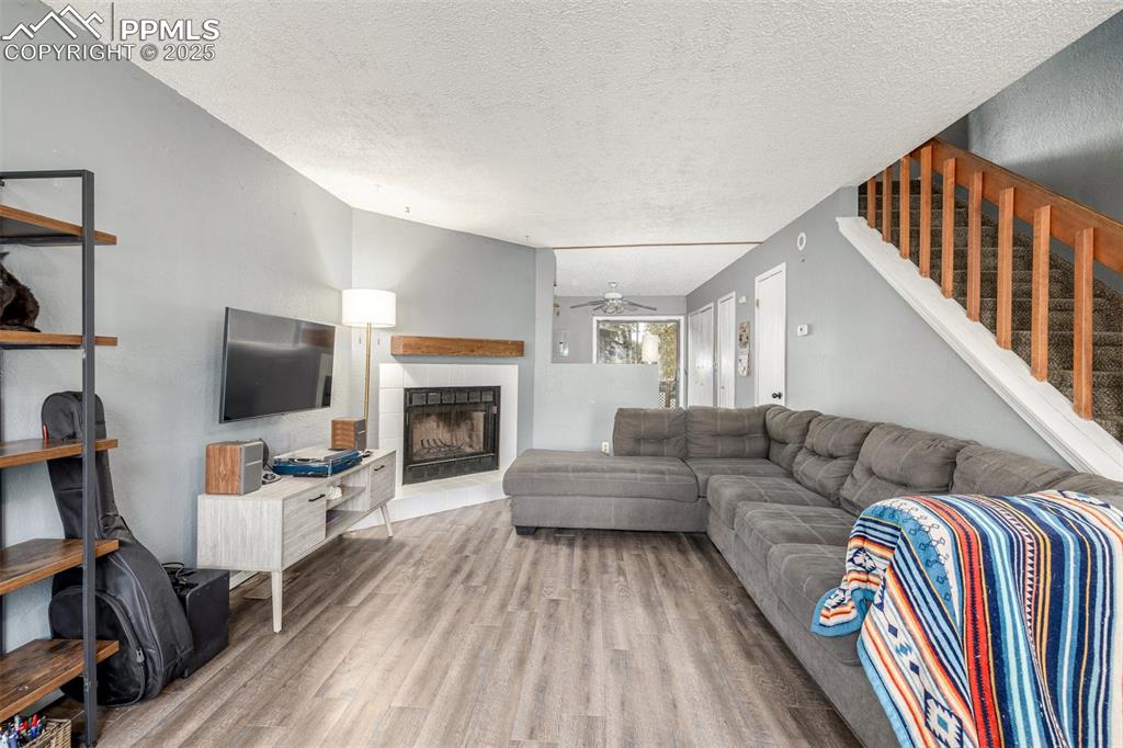 Living room featuring a tile fireplace, light wood-type flooring, a textured ceiling, and ceiling fan