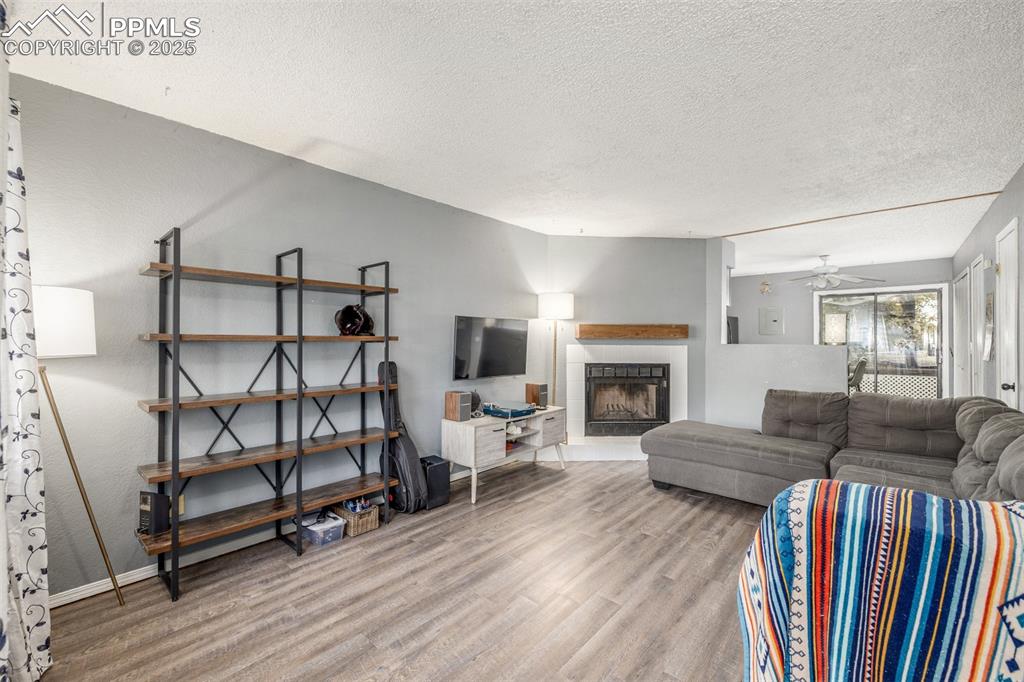 Living room featuring wood finished floors, a tiled fireplace, ceiling fan, and a textured ceiling