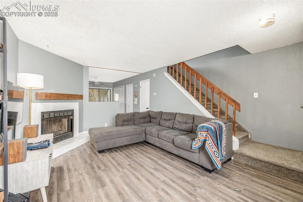 Living area with a tiled fireplace, a textured ceiling, stairway, wood finished floors, and a ceiling fan