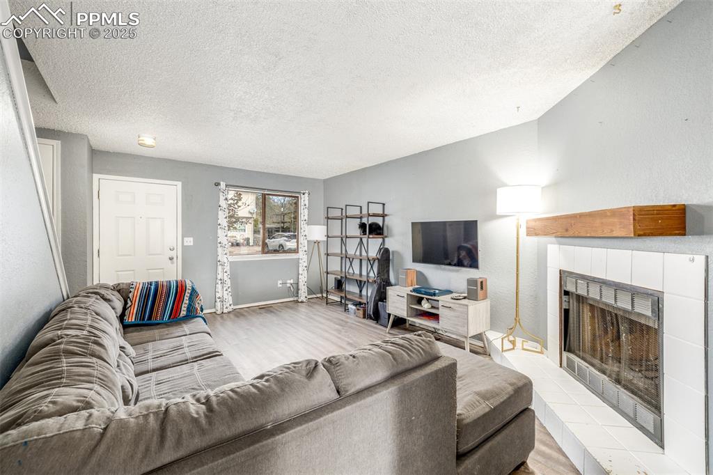 Living area with a tile fireplace, wood finished floors, a textured ceiling, and a textured wall