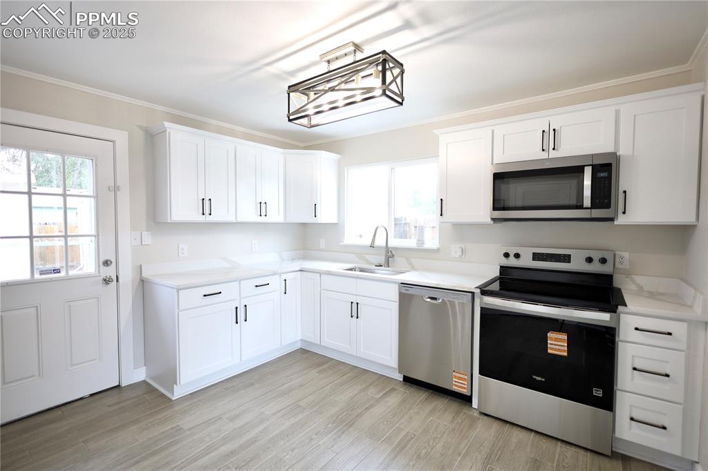 Kitchen featuring stainless steel appliances, white cabinetry, light wood-style flooring, and ornamental molding
