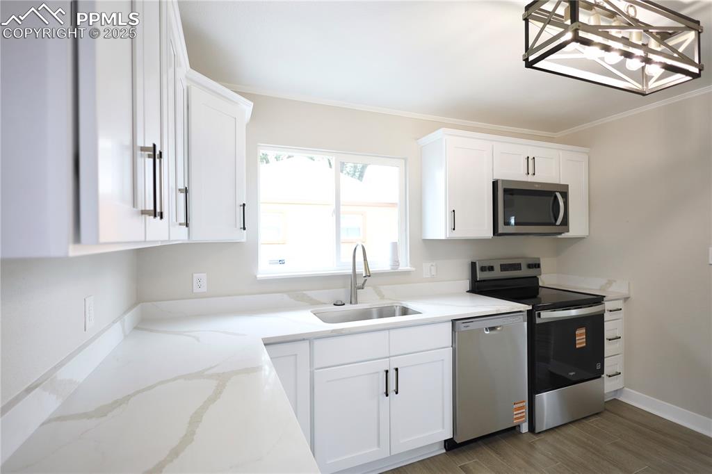 Kitchen with white cabinetry, stainless steel appliances, crown molding, light stone counters, and dark wood-type flooring