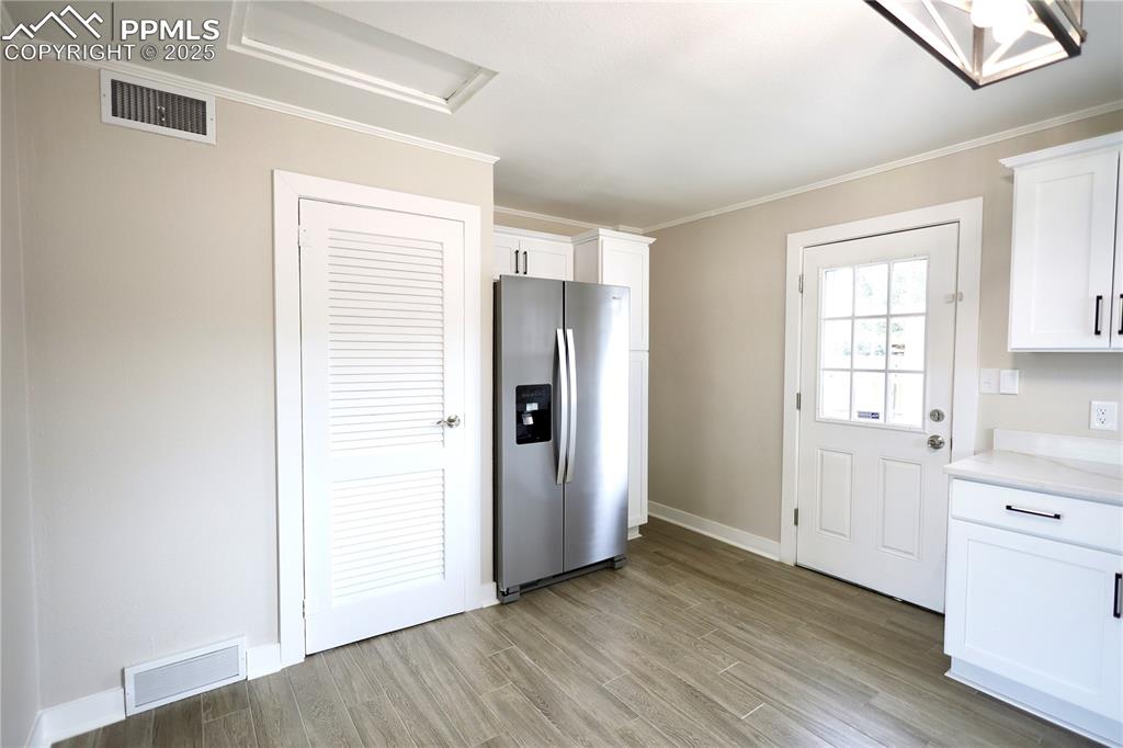 Kitchen with stainless steel refrigerator with ice dispenser, white cabinetry, ornamental molding, and light wood-style flooring